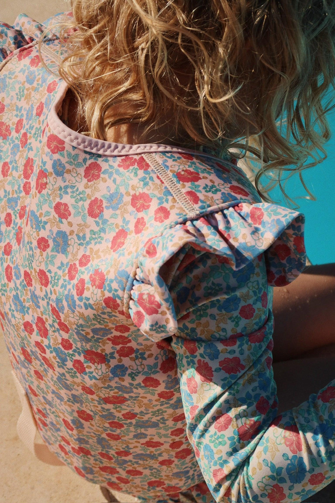 The little girl is wearing a rashguard with pastel florals on the suit: blue and red/coral flowers. 
