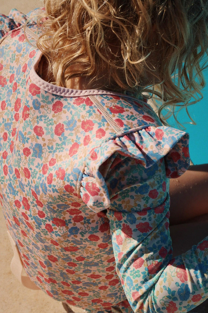 The little girl is wearing a rashguard with pastel florals on the suit: blue and red/coral flowers. 