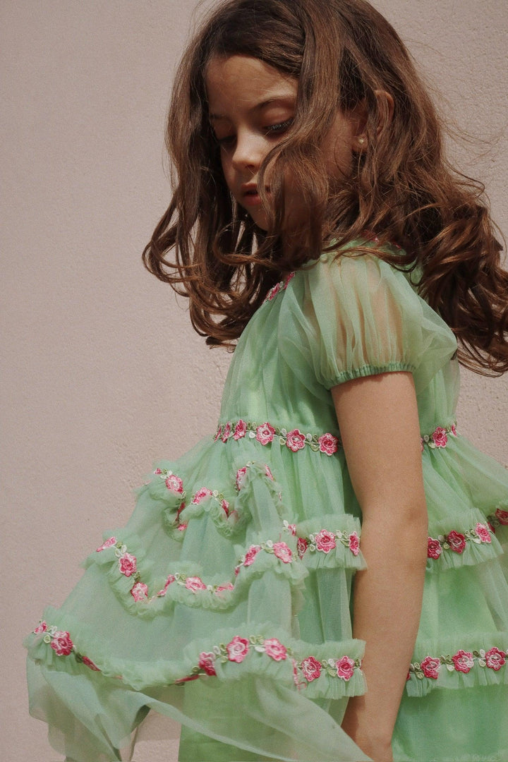 little girl wearing the green tulle dress with pink floral appliques as stripes all along the bottom of the dress. 