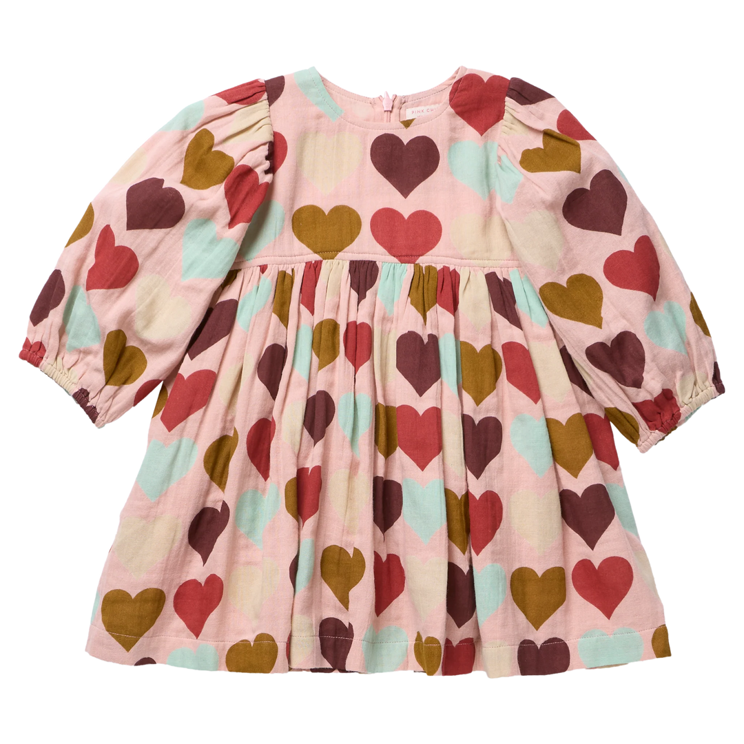 A pink long-sleeve baby dress with a pattern of red, brown, and mint green hearts, featuring puffed sleeves and a gathered waist.
