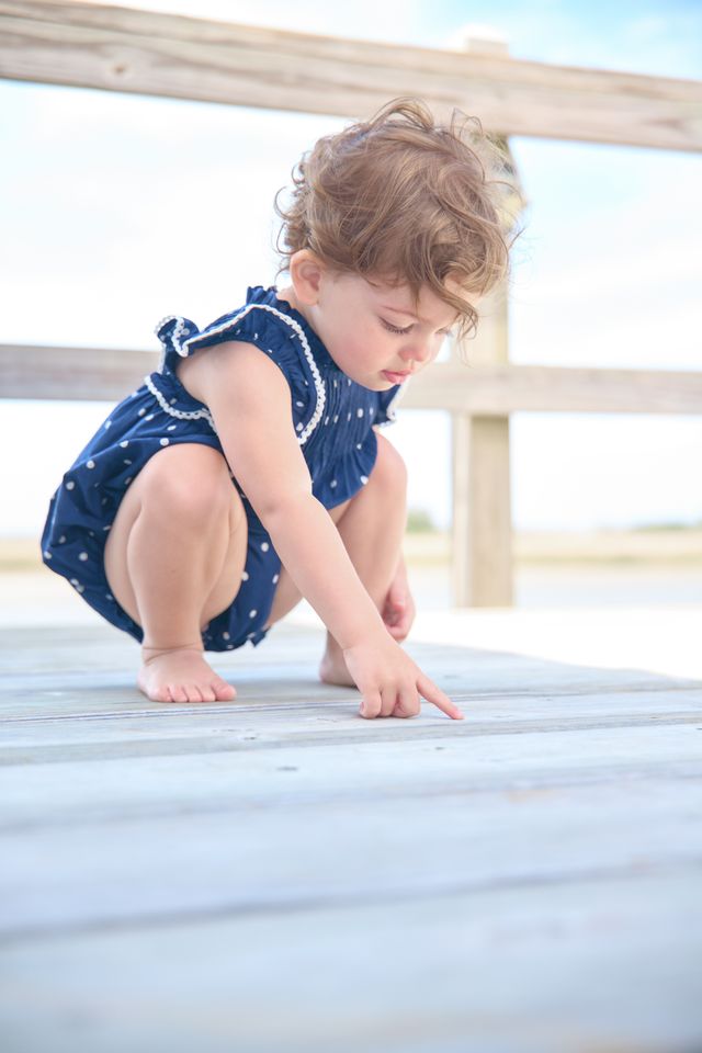 Child in a blue dress playing on a wooden deck.
