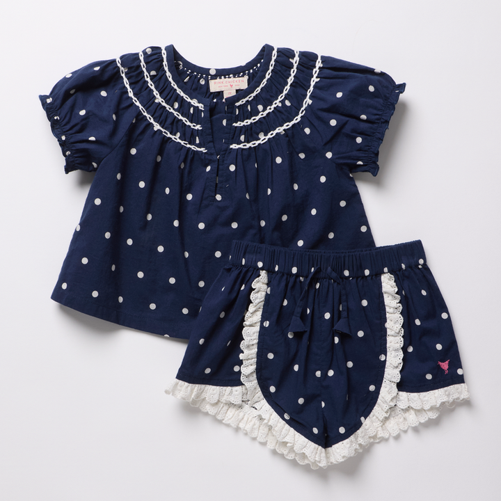 Navy blue top and shorts set with white polka dots and ruffles on a light gray background