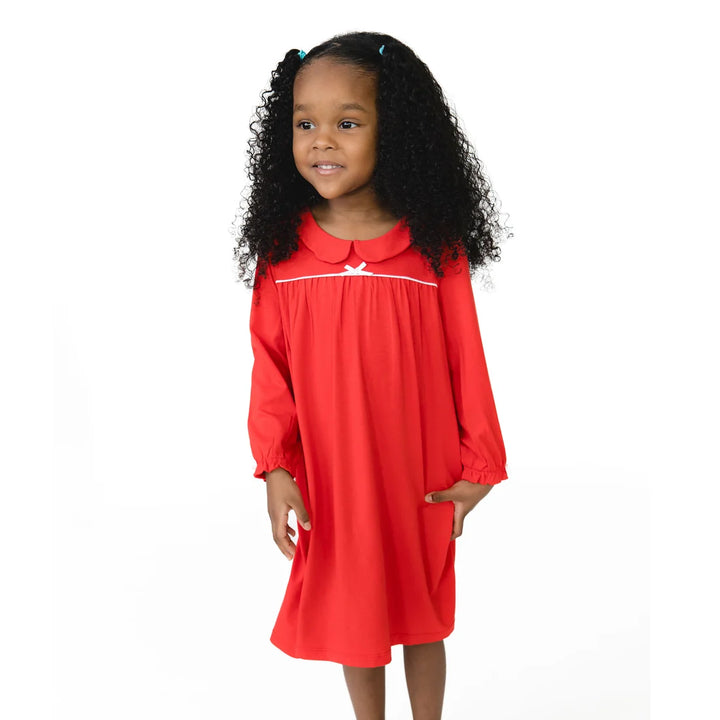 A young girl with curly black hair wearing a bright red long-sleeve dress with a white collar trim and a small white bow, standing against a plain white background.