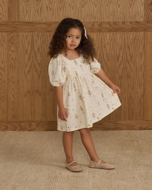 Young girl in a nutcracker dress standing against a wooden paneled wall.