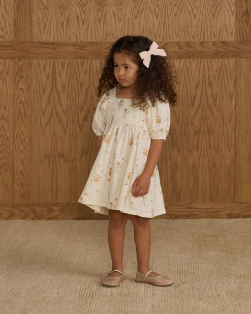 Young girl in a nutcracker dress standing against a wooden paneled wall.