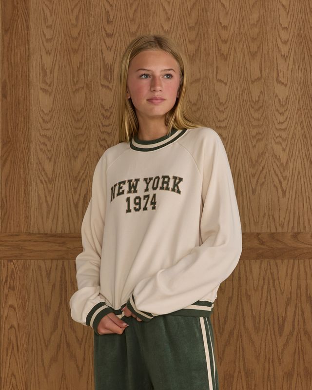 Person wearing a 'New York 1974' sweatshirt against a wooden paneled wall.