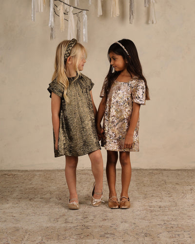 two little girls posing in sparkly dresses, one is gold foil and one is sequin with short sleeve. 