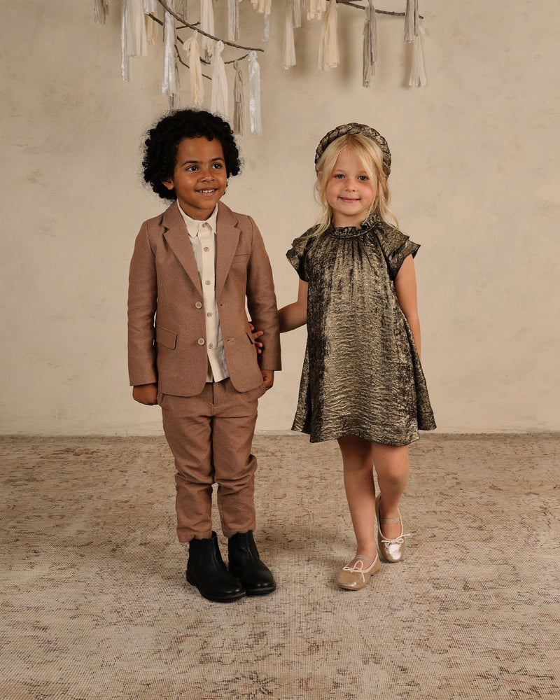 little girl posing with little boy both are dressed up in evening attire. little girl is wearing our Isabella dress that is made of a gold foil  aline silhouette. 