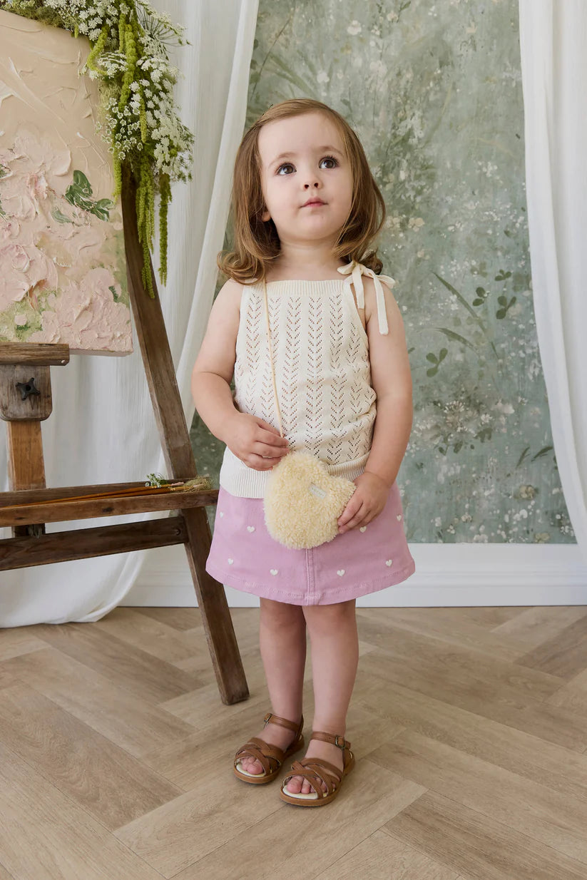 Young girl in a knitted top and pink skirt standing in a room with floral decor.