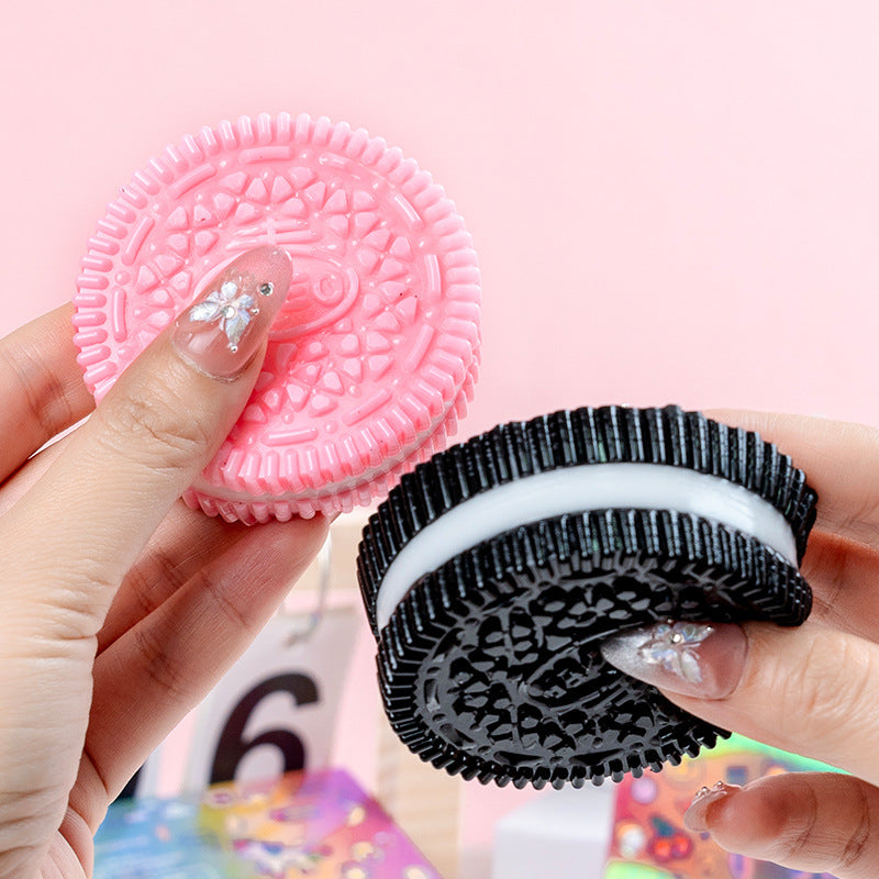 Pink and black oreo cookie-shaped squish toy held by a hand against a pink background