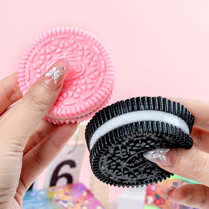 Pink and black oreo cookie-shaped squish toy held by a hand against a pink background