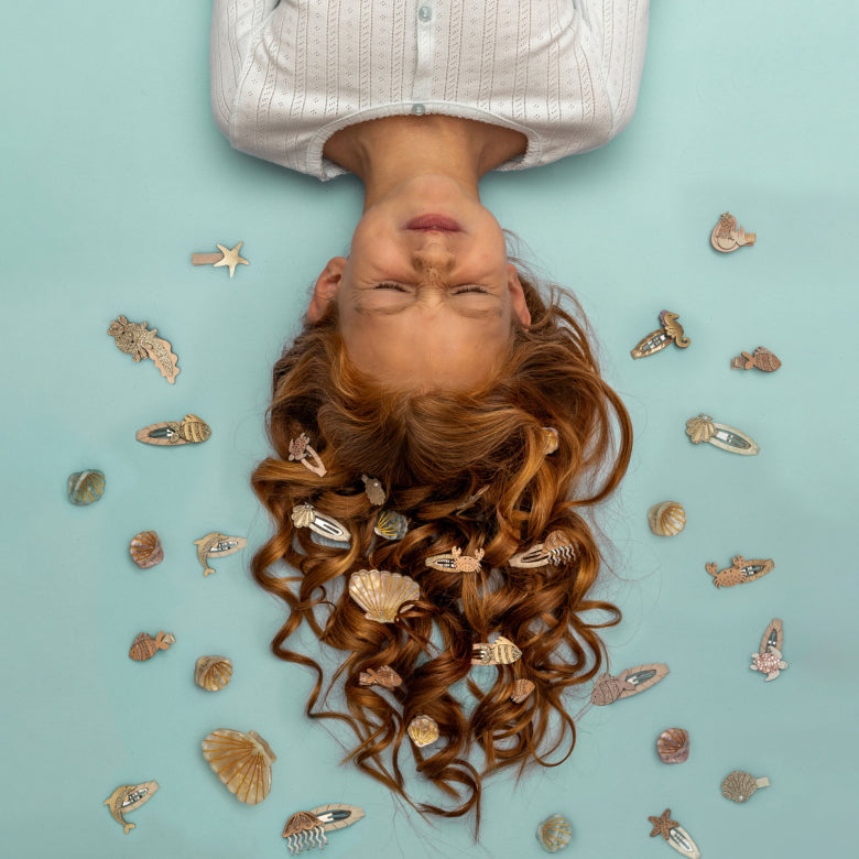 Person with long red hair lying on a light blue background with decorative  hair clips