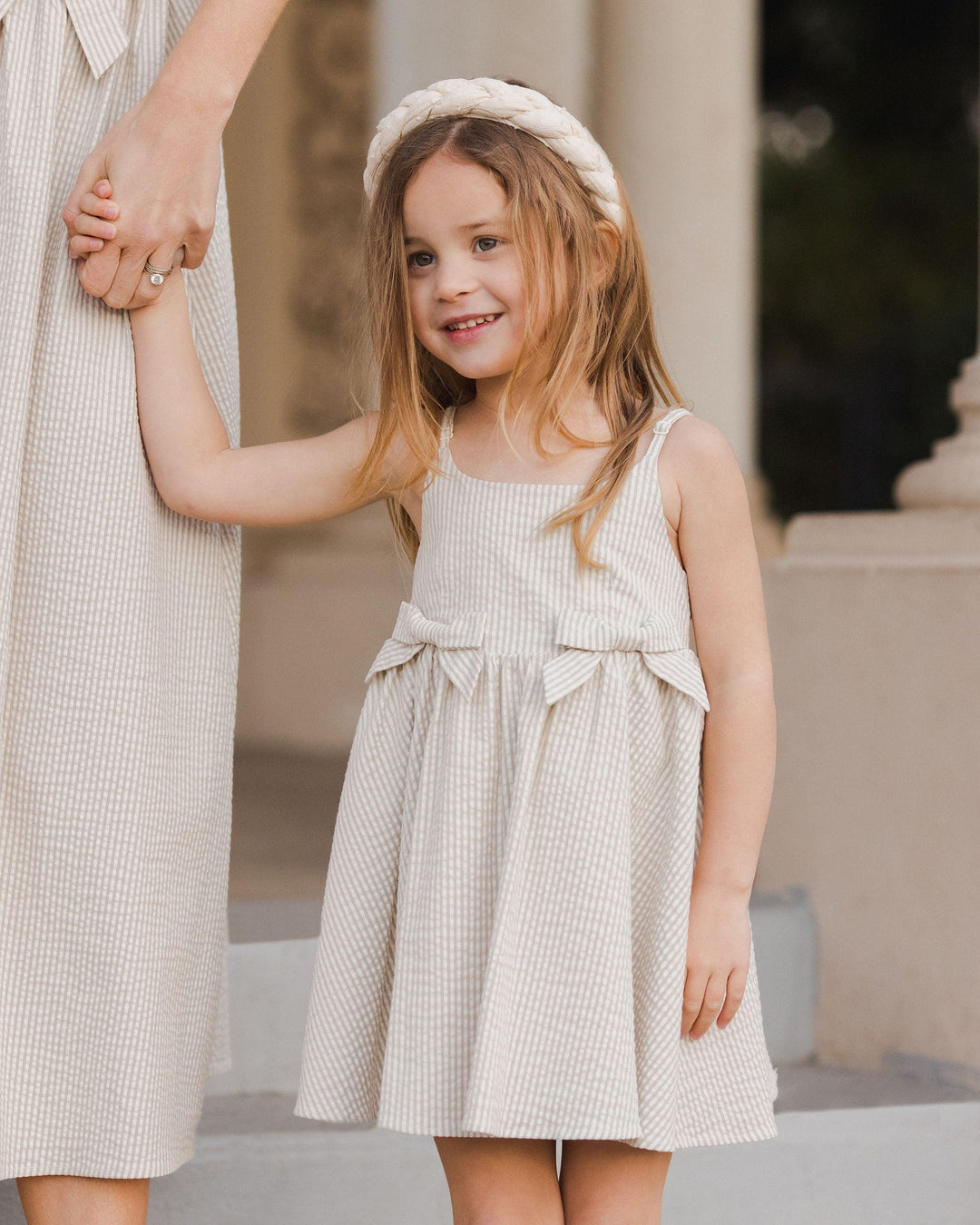 little girl holding her mother's hand while wearing the sage stripe dress and full skirt. 