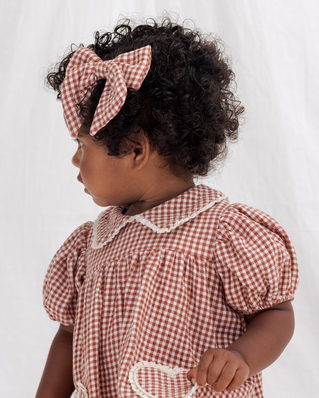 Child wearing a red and white checkered dress with a matching headband on a white background