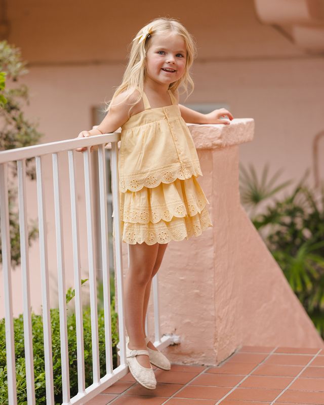 Young girl in a yellow two piece outfit with eyelet detailing standing on a balcony