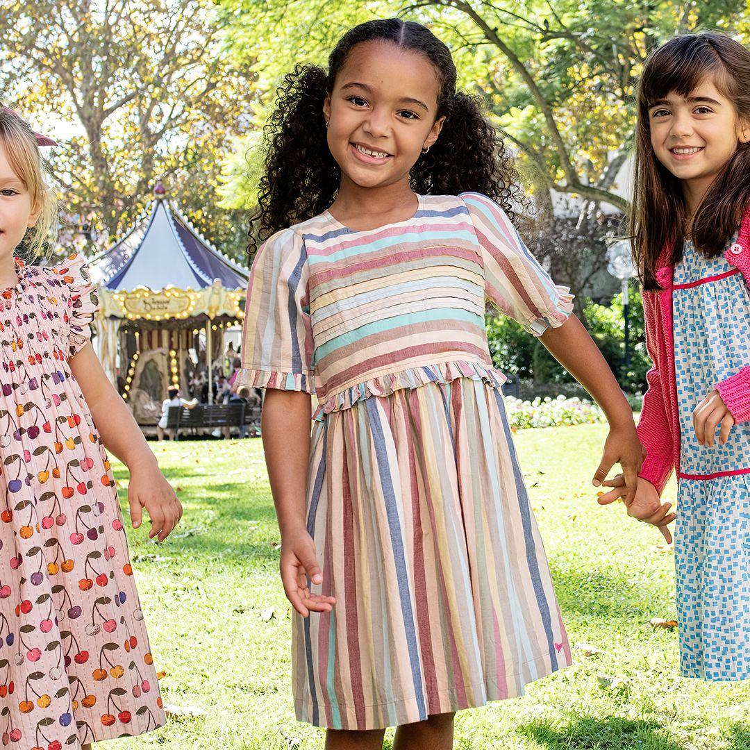 this picture shows the young girl modeling the muted pastel striped dress with two other girls in the park