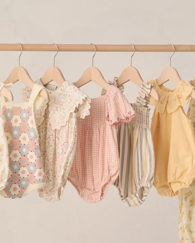 Collection of baby rompers on hangers against a neutral background