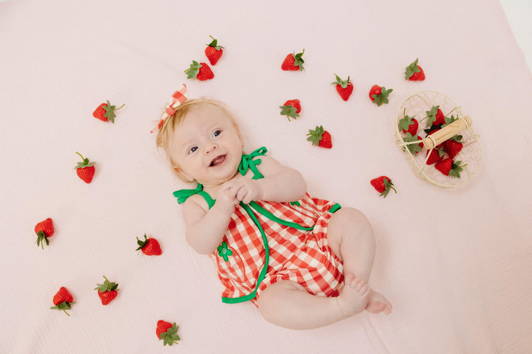 baby laying down in the red and white gingham check sunsuit with green trim . 