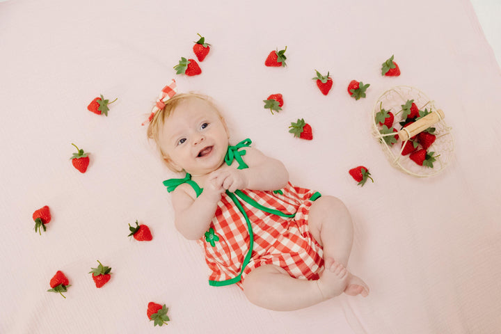 baby laying down in the red and white gingham check sunsuit with green trim . 