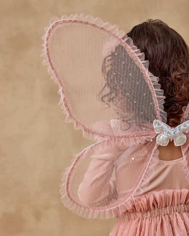 Person wearing a pink fairy costume with butterfly wings on a beige background