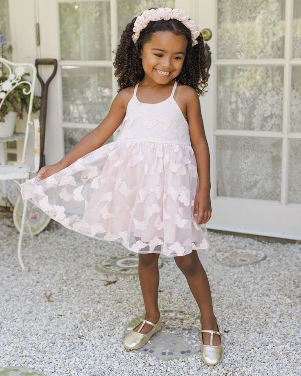 Young girl in a light pink floral dress standing outdoors near a white door.