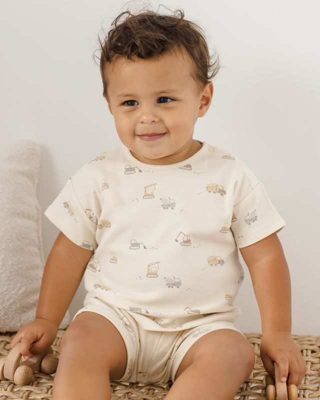 Baby wearing a white onesie with car patterns on a light background
