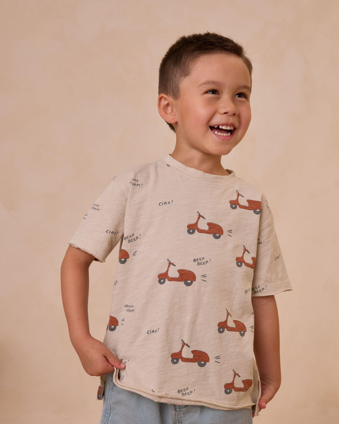 young boy modeling the raw edge tee with brick red mopeds printed all over it 