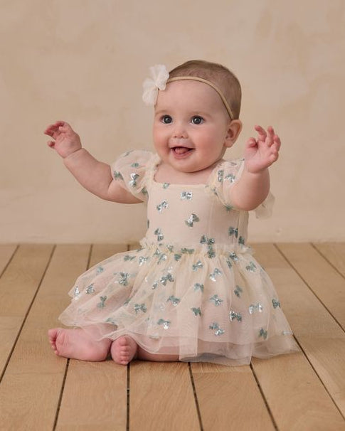 Baby in a floral dress sitting on a wooden floor with a beige background