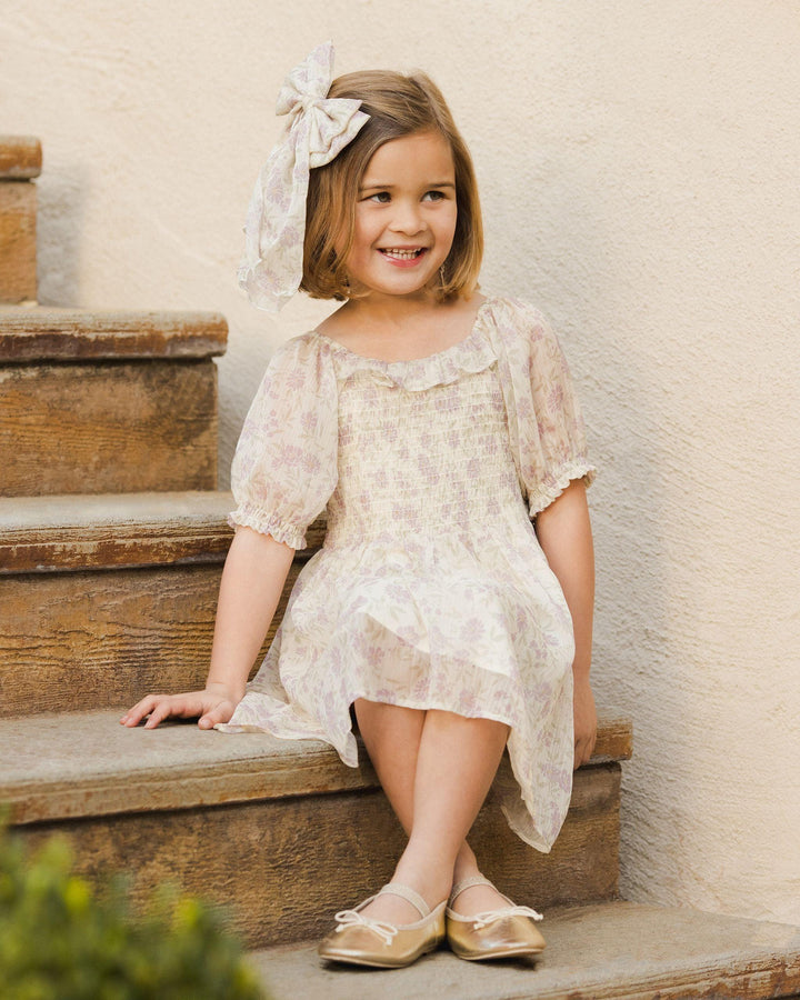 little girl sitting on the steps wearing the millie dress in the lavender field color way. it looks delicate and light. provides coverage to the knee and elbow 