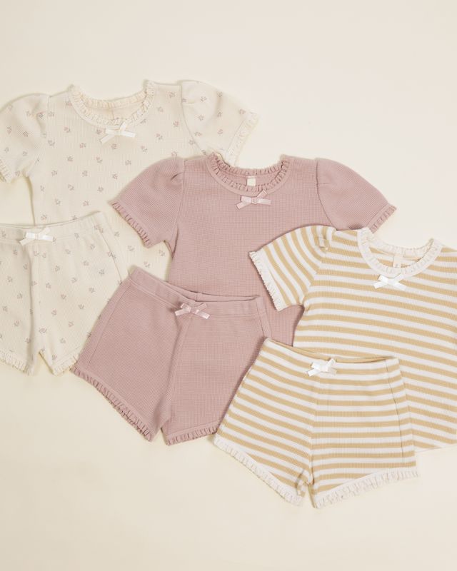 Children's clothing set with pink top and shorts, and yellow striped shirt and shorts on a beige background.
