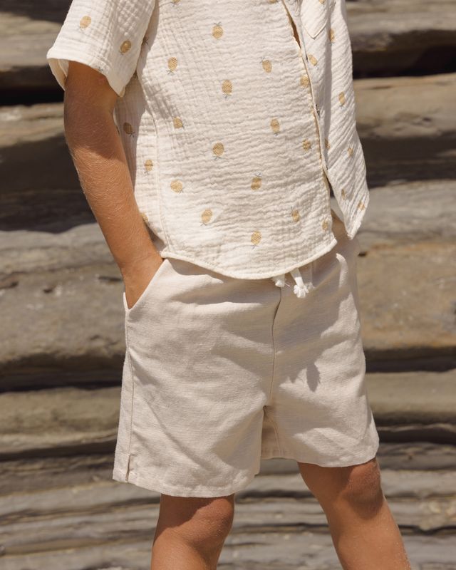 Person wearing a beige patterned shirt and shorts standing on wooden planks.