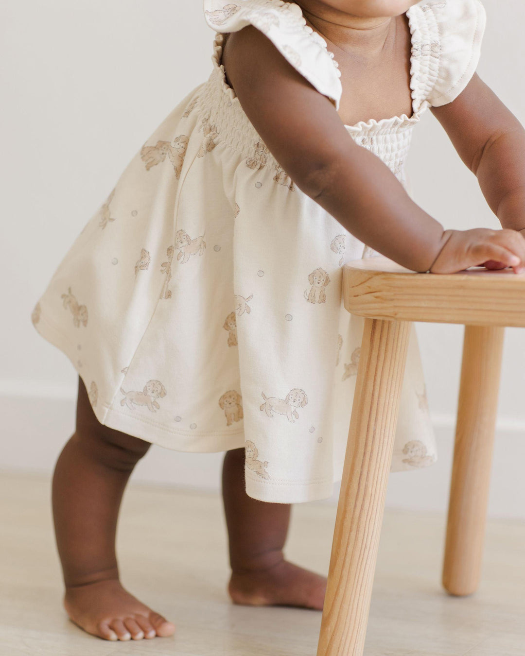 baby modeling the beige puppy dress. tiny brown dogs all over the dress.  hits just above the knee