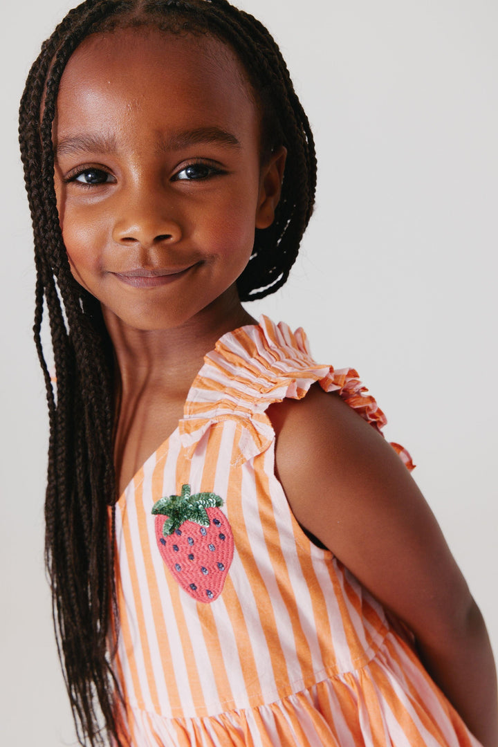 close up look at the strawberry embellishement on the on dress while a little girl is modeling it. 