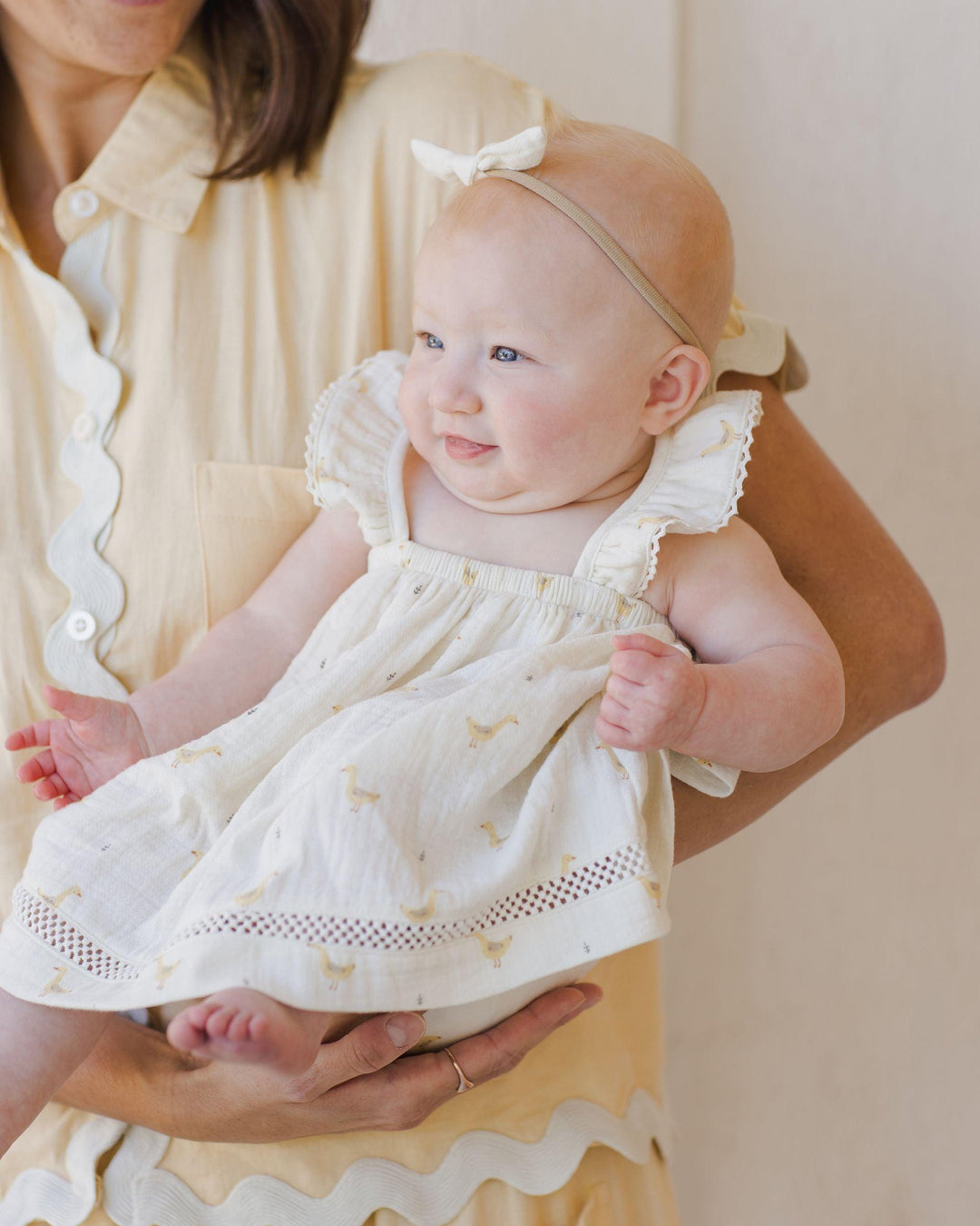 the mom is holding baby and the baby is sitting in her arms. The baby's dress folds over the arm and the baby looks happy . 