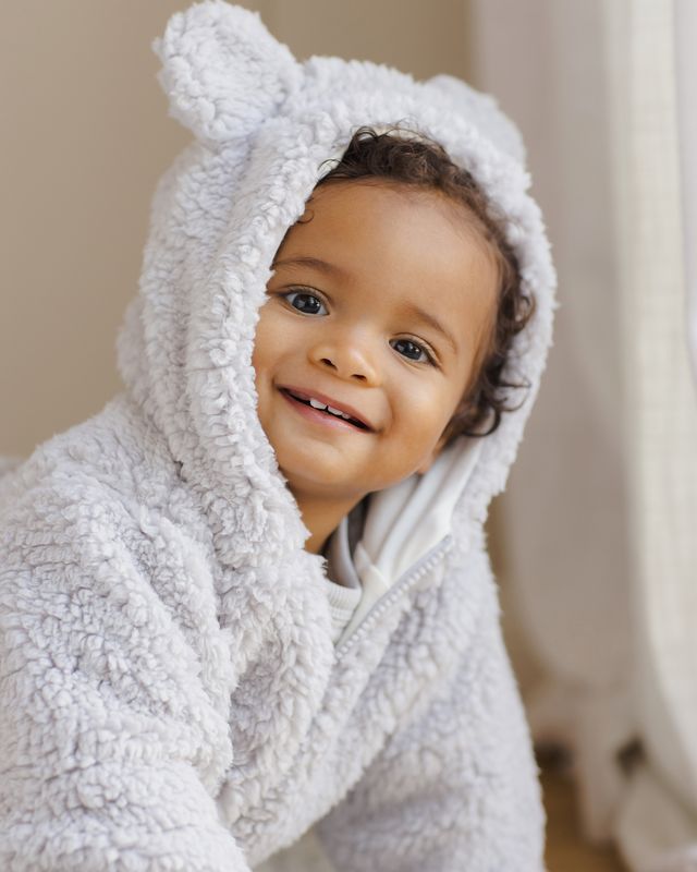 Child wearing a white hooded towel with bear ears, smiling indoors.