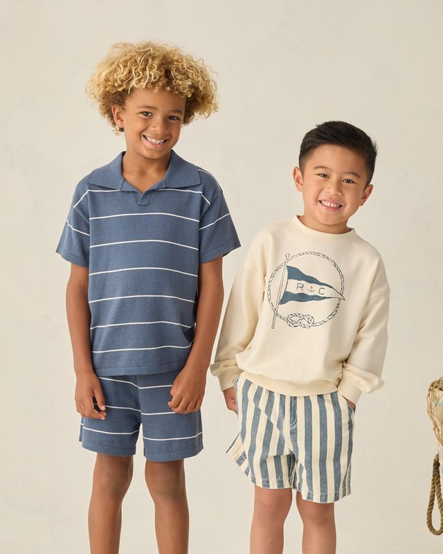 Two children wearing matching blue and white striped outfits on a plain background