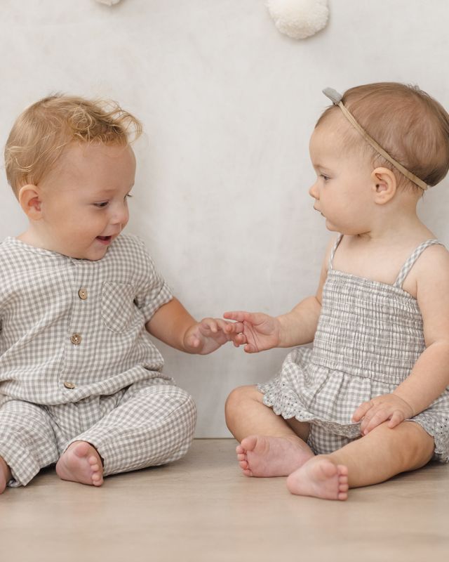 Two toddlers in matching checkered outfits sitting on a wooden floor.