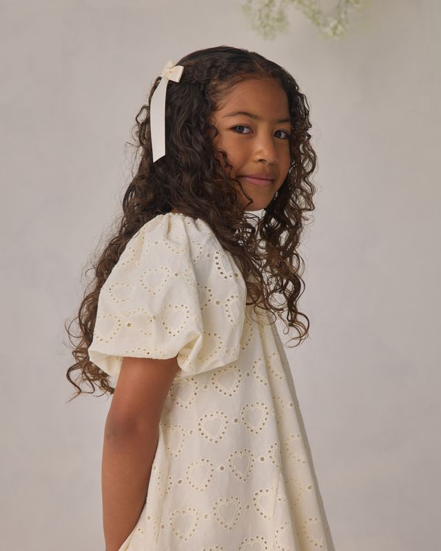 Young girl wearing a white dress with a subtle pattern against a plain background