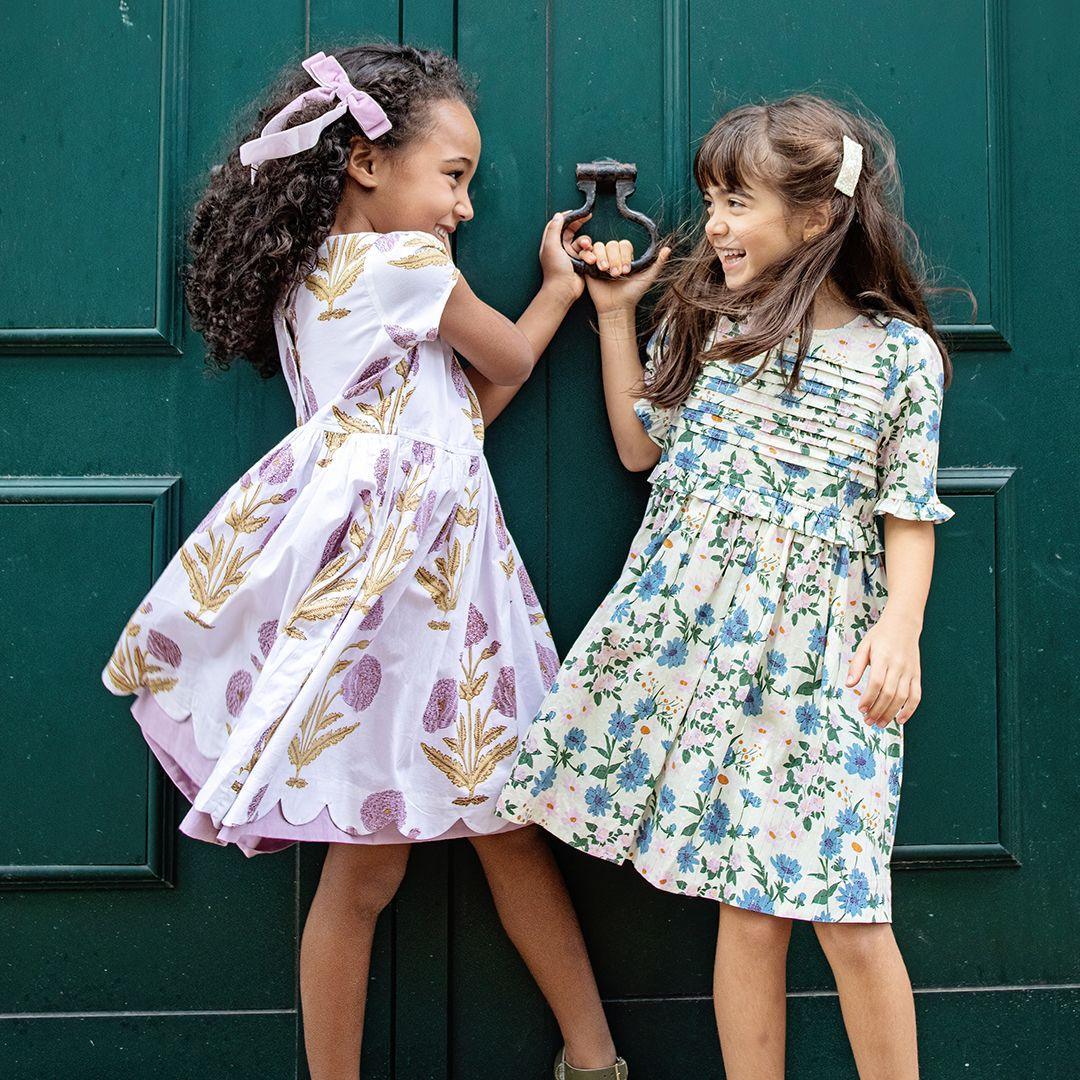 youngs girls laughing and wearing the same two dresses: lavender and white and white and blue flowers. 