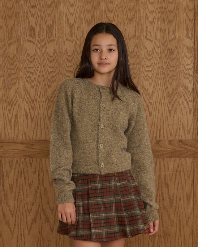 young girl wearing a green cardigan and pleated plaid skirt 