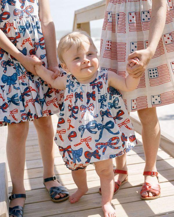 picture of baby wearing the bows that have a stars and stripes pattern inside the bow. there is also a slightly older girl wearing the dress as well. 