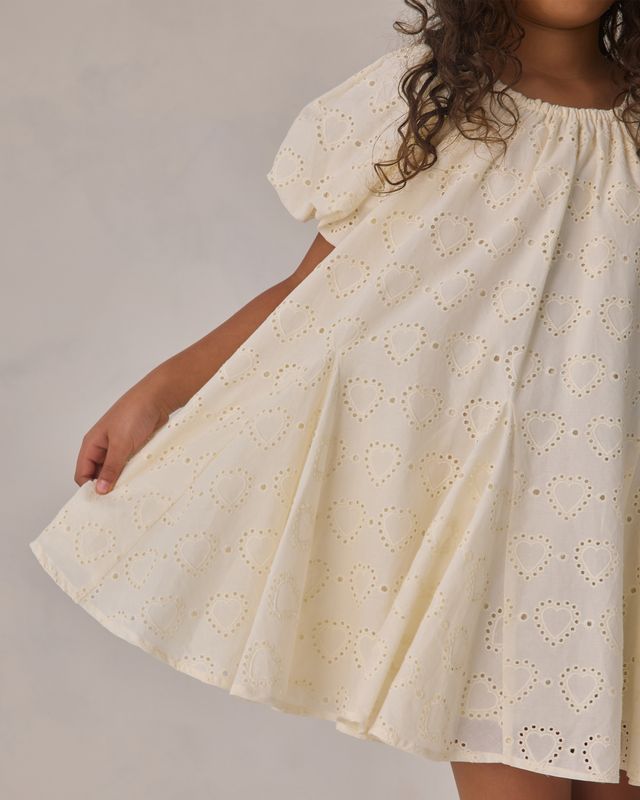 White dress with heart pattern worn by a child on a plain background