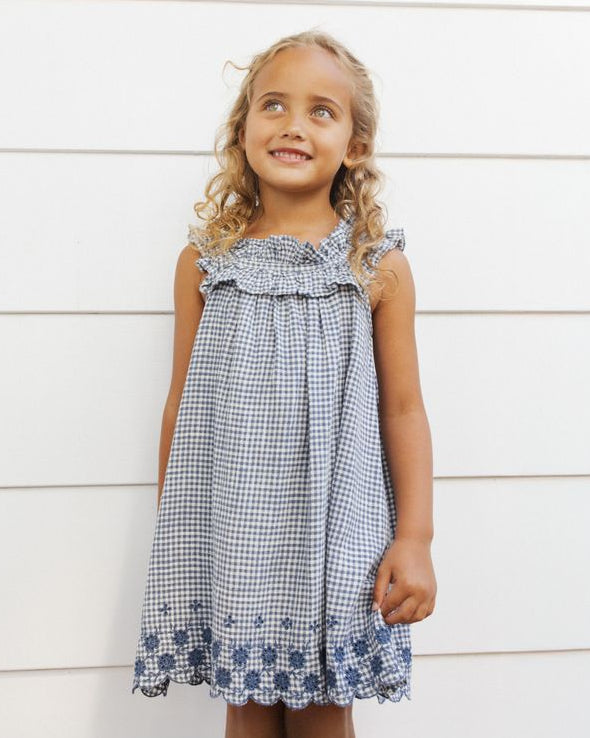 Young girl wearing a blue checkered dress against a white wooden background
