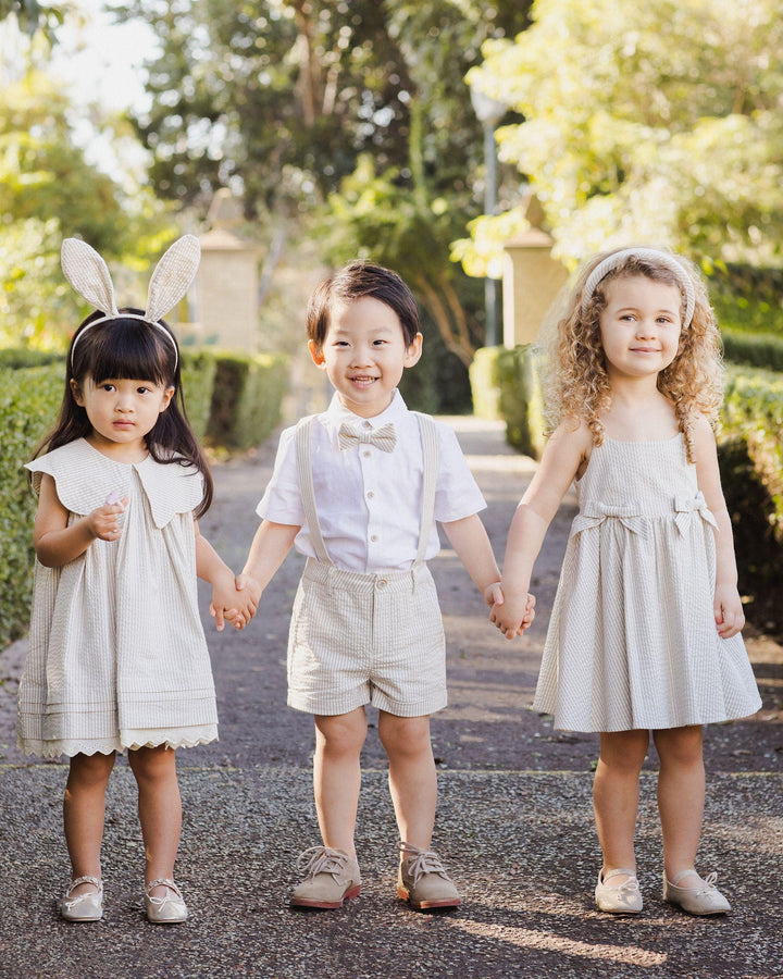 three small children holding hands all dressed up. the little girl on the right is in the sage stripe dress and full skirt. 