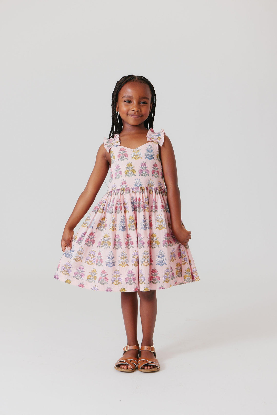 little girl wearing the pink dress with boho floral print. she is holding the skirt to show the potential movement in the skirt