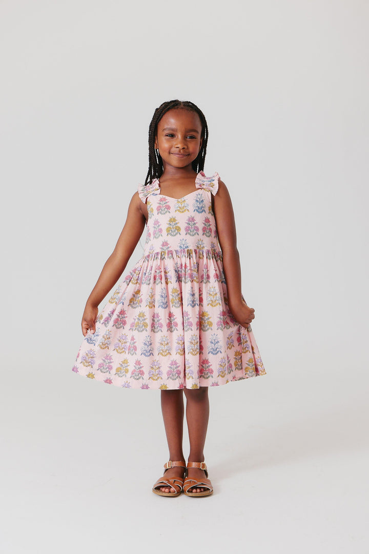 little girl wearing the pink dress with boho floral print. she is holding the skirt to show the potential movement in the skirt