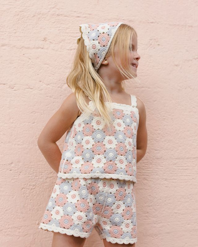 Young girl wearing a floral crochet outfit against a pink brick wall.