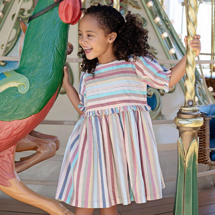 young girl modeling the muted pastel stripes dress. it shows the dress knee length and with a full skirt