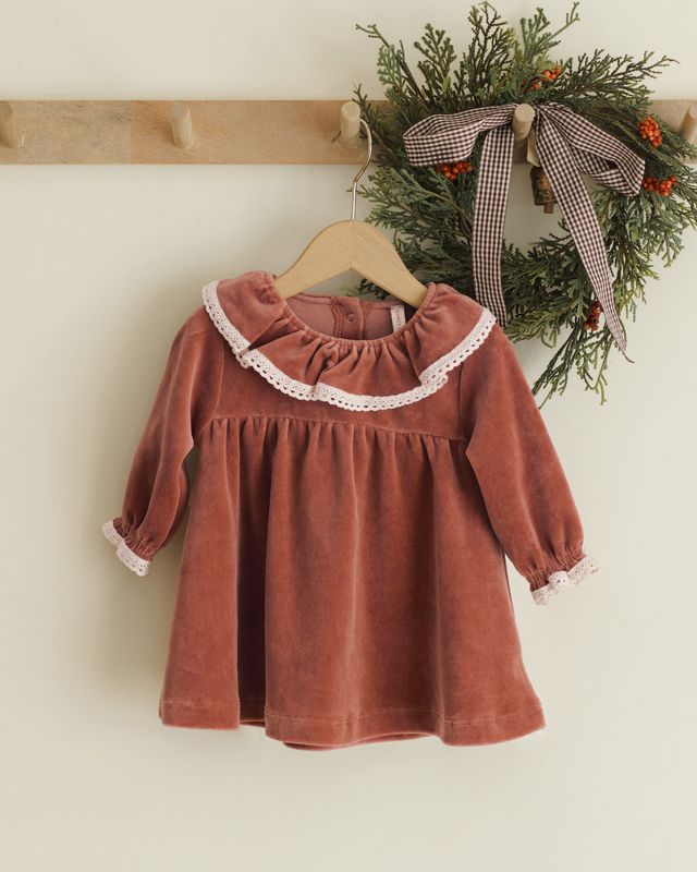Children's rust-colored dress with lace trim on a wooden hanger against a neutral background.