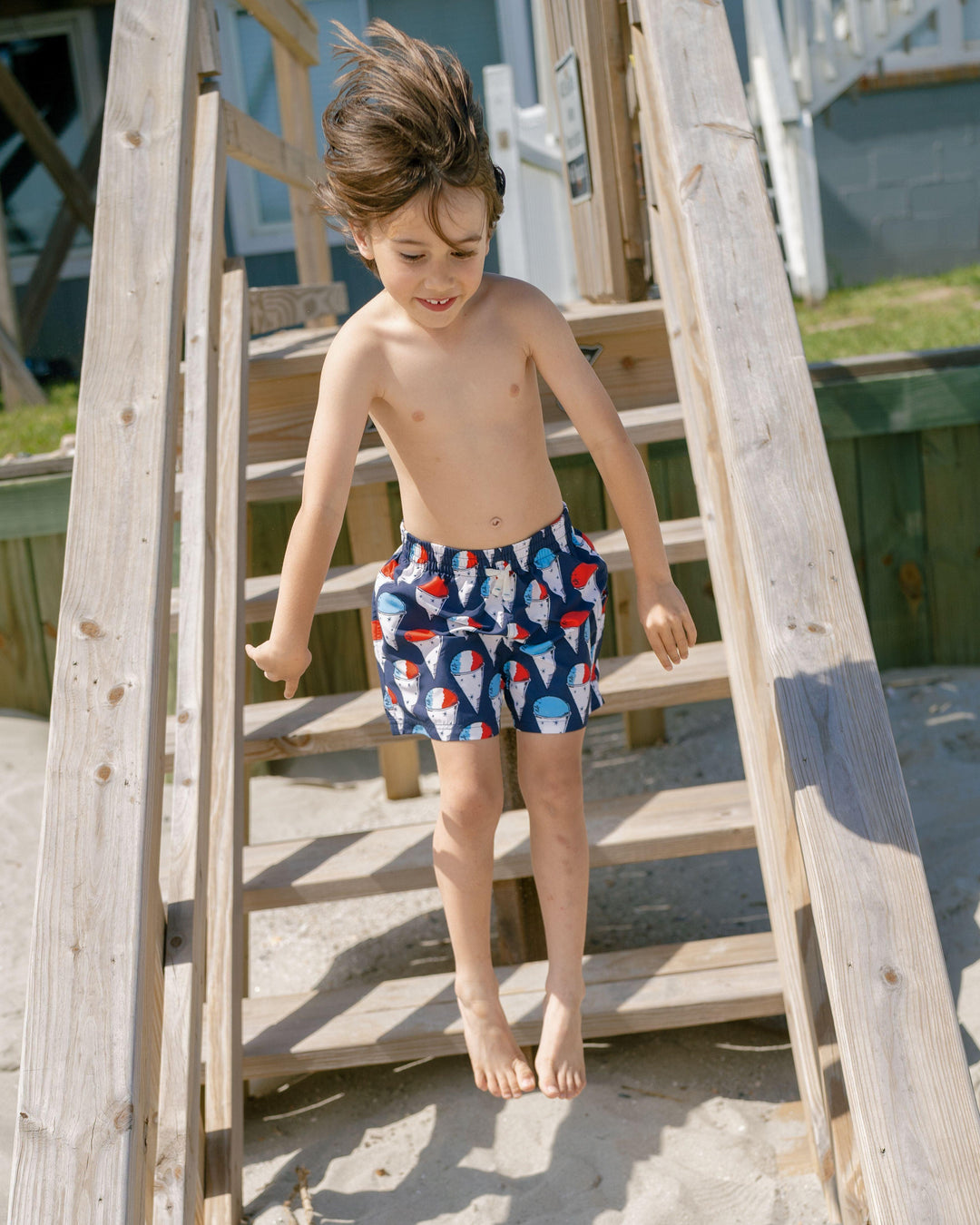 little boy modeling the swim trunks, navy base with red, white and blue snow cones printed all over the swim trunks. 